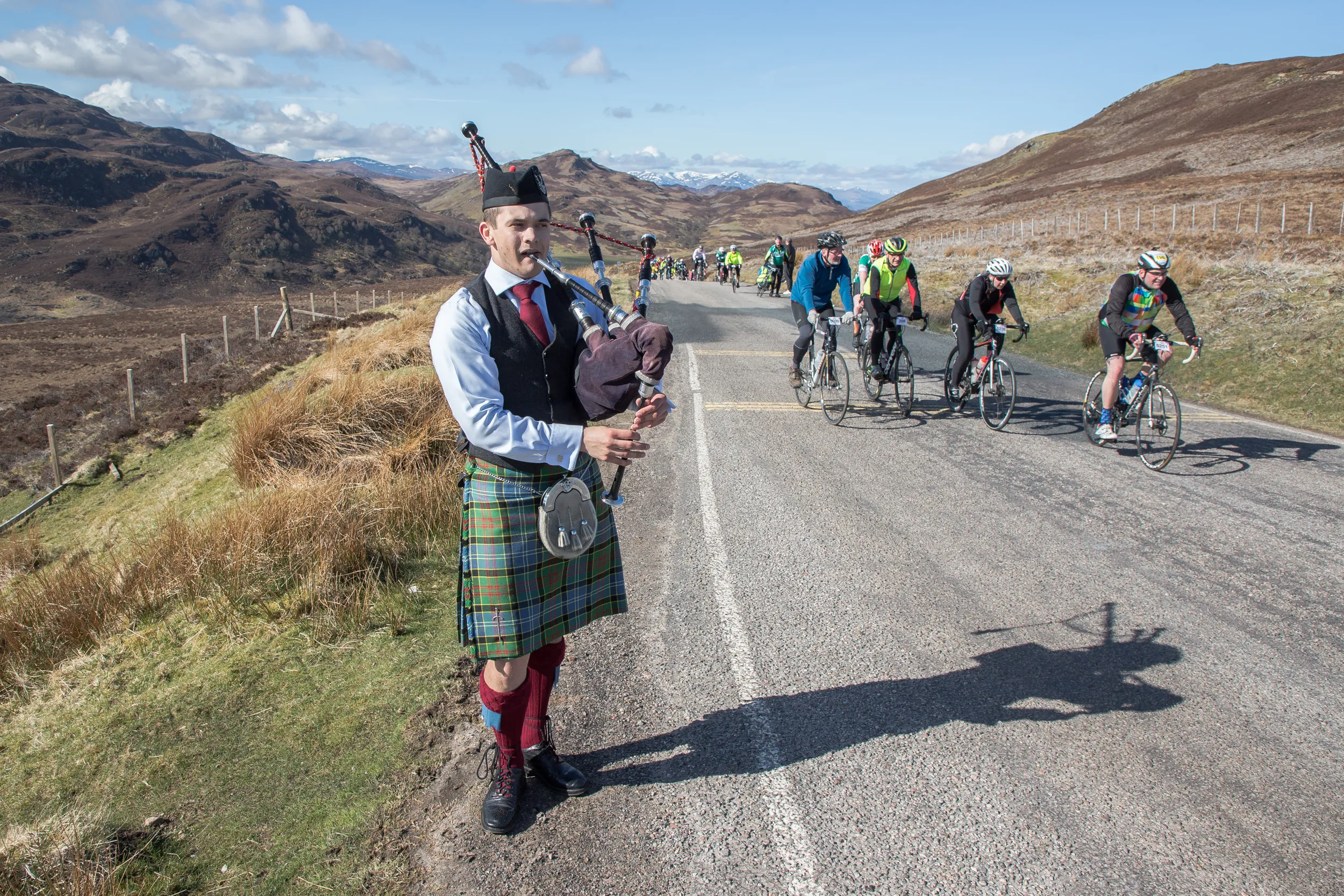 A bagpiper plays for riders going past